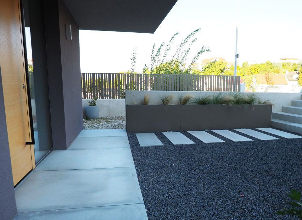 Rechteckige Gehwegplatten aus Beton und großformatige Bodenplatten in Zementgrau mit schalreiner Oberflächenstruktur